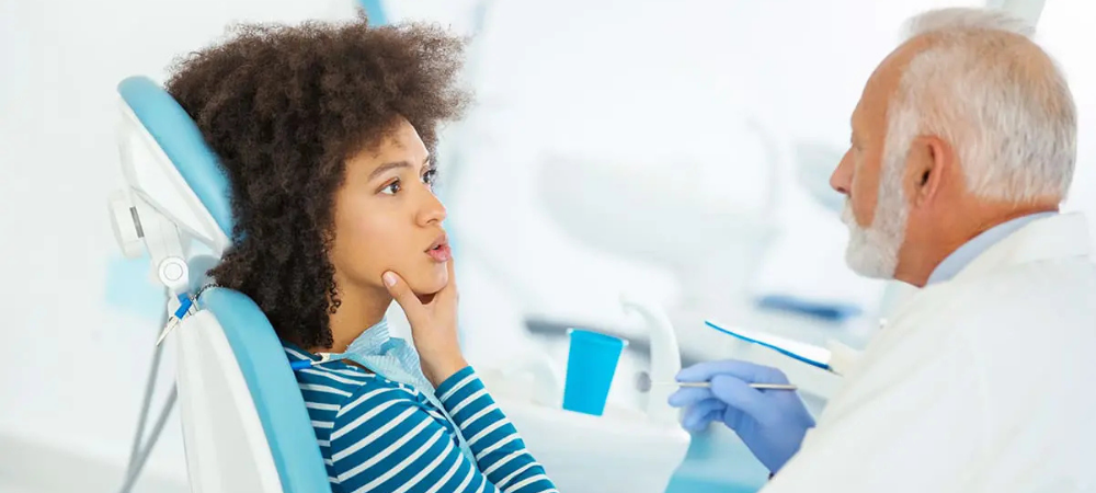 woman at the dentist, explaining jaw pain with her hand on her jaw