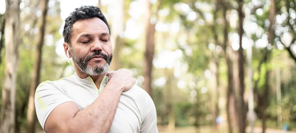 man in the forest with hand on shoulder, signifying pain