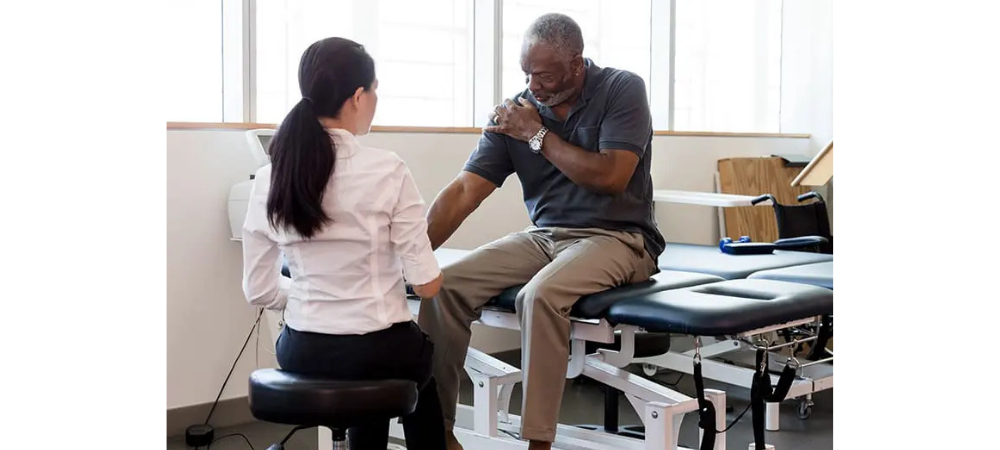 patient with shoulder pain sitting on treatment table, doctor evaluating him