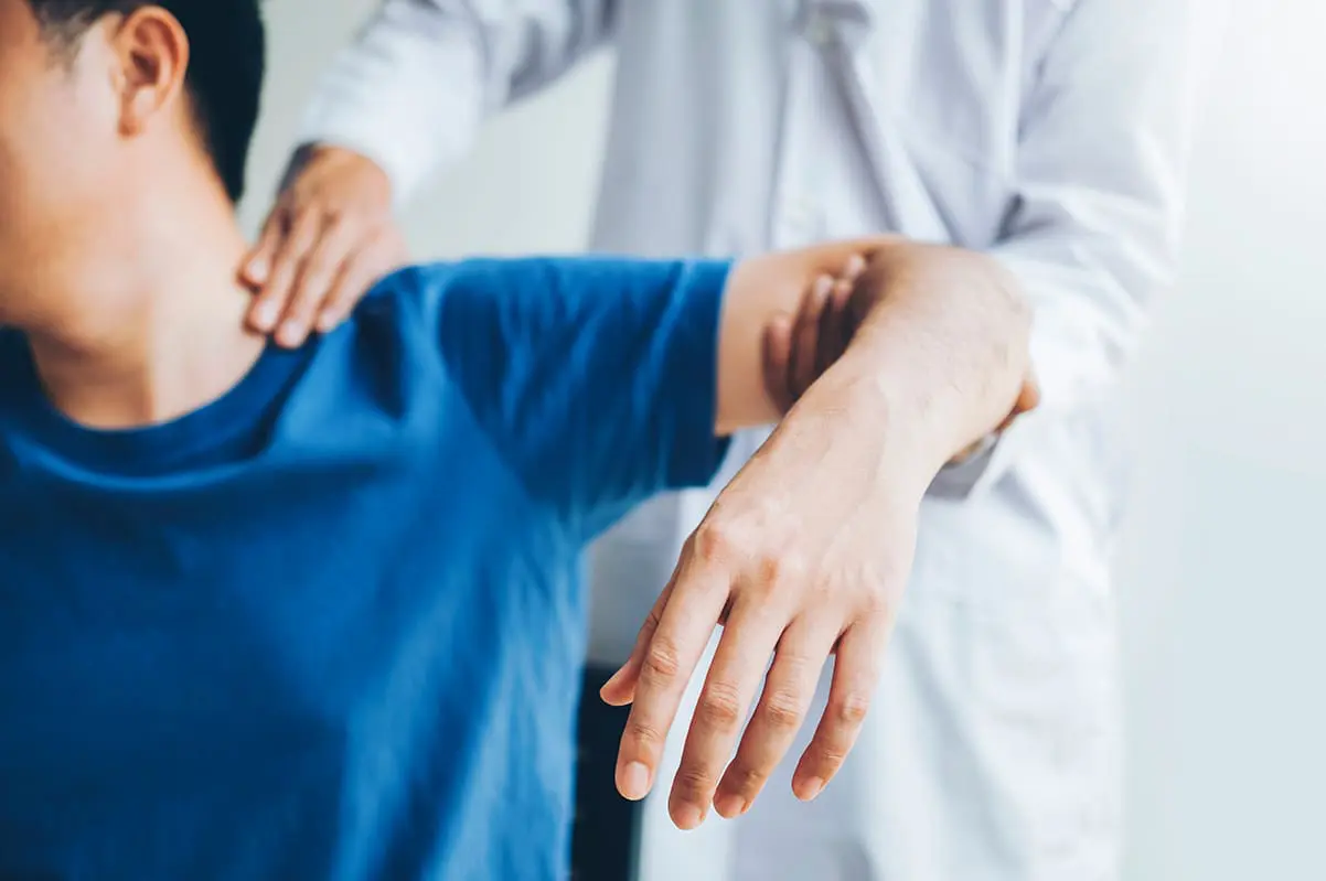 man sitting with arm raised, doctor behind him