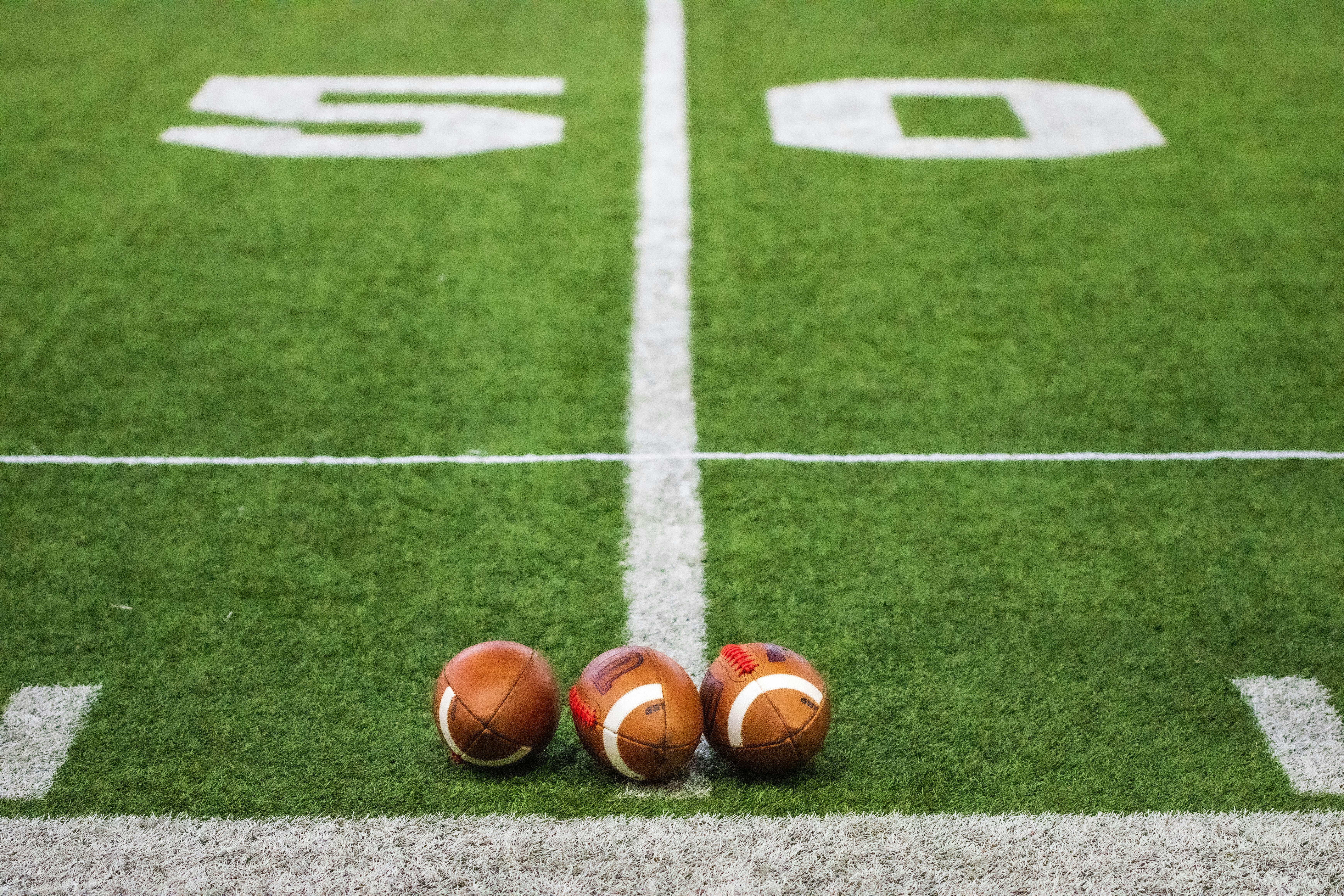 football field with three footballs sitting on the grass